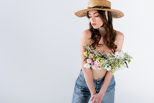 Young woman in straw hat, jeans and flowers in blouse isolated on grey