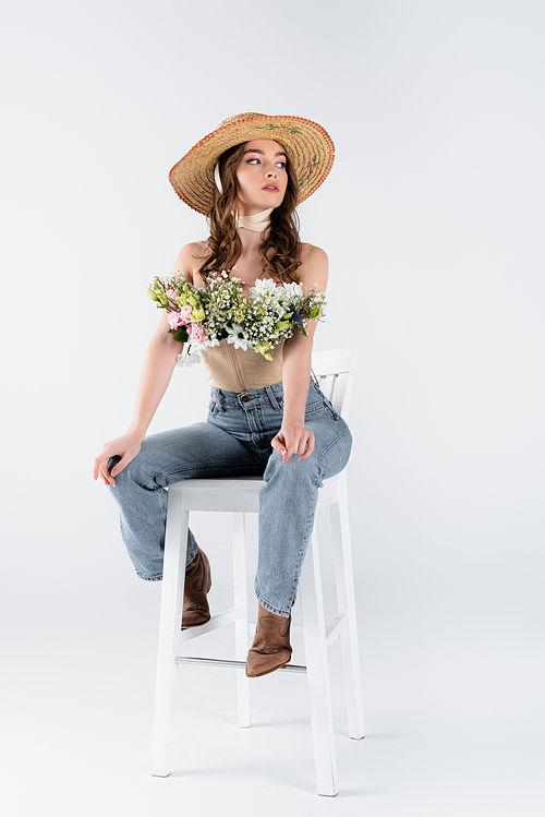 Stylish model with flowers in blouse posing on chair on grey background