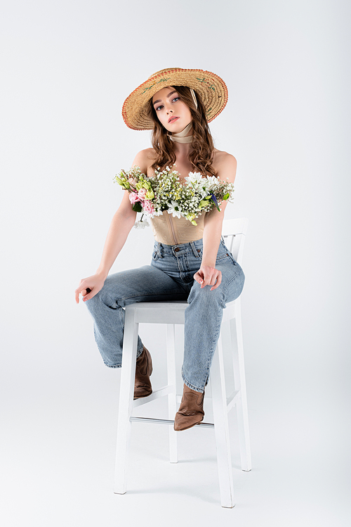 Woman with bouquet in blouse  while sitting on chair on grey background