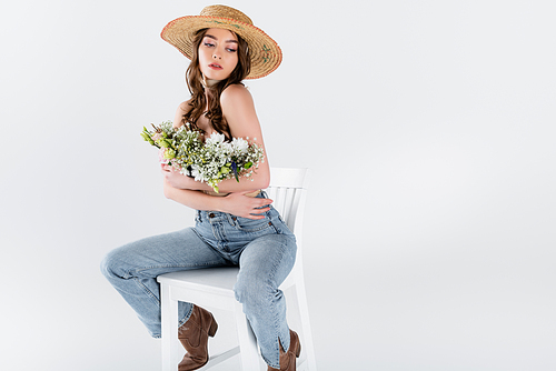 Stylish woman hugging flowers while sitting on chair isolated on grey