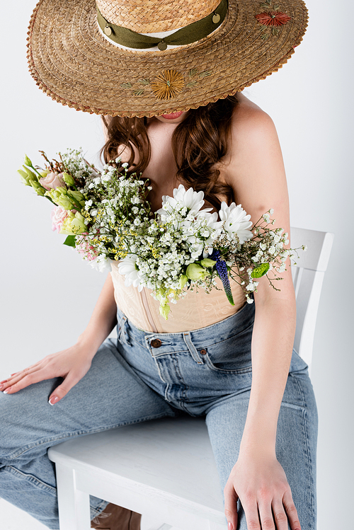 Straw hat covering face of woman with flowers in blouse isolated on grey