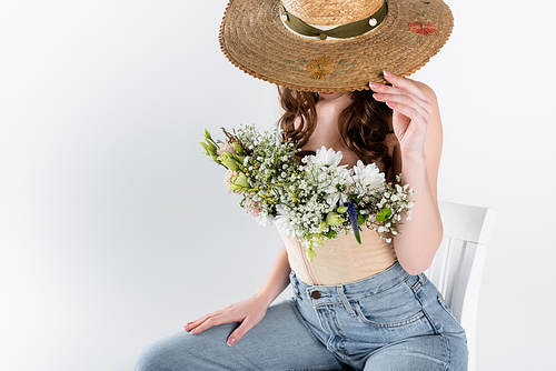 Woman with flowers in blouse covering face with sun hat isolated on grey