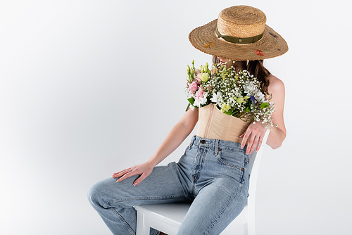 Woman with flowers in blouse and sun hat sitting on white chair isolated on grey