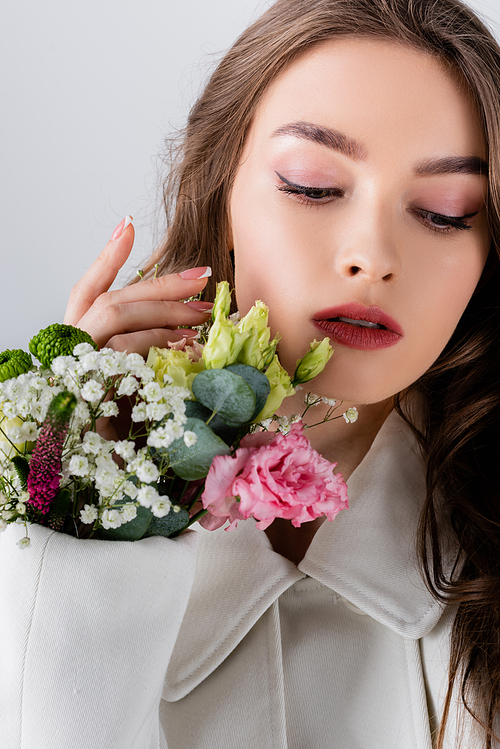 Brunette woman with flowers in sleeve of coat looking away isolated on grey