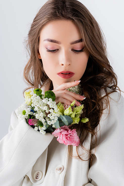 Brunette model posing with flowers in sleeve of coat isolated on grey