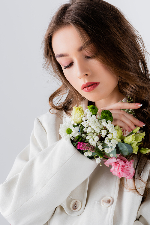 Young model in coat with flowers in sleeve standing isolated on grey