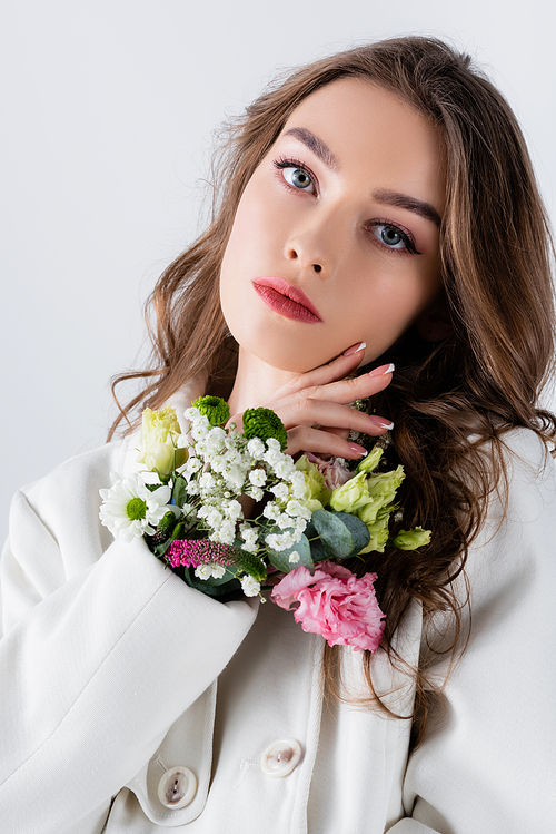 Young model  near different flowers in sleeve of coat isolated on grey
