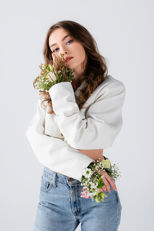 Young model with flowers in sleeves of jacket posing isolated on grey