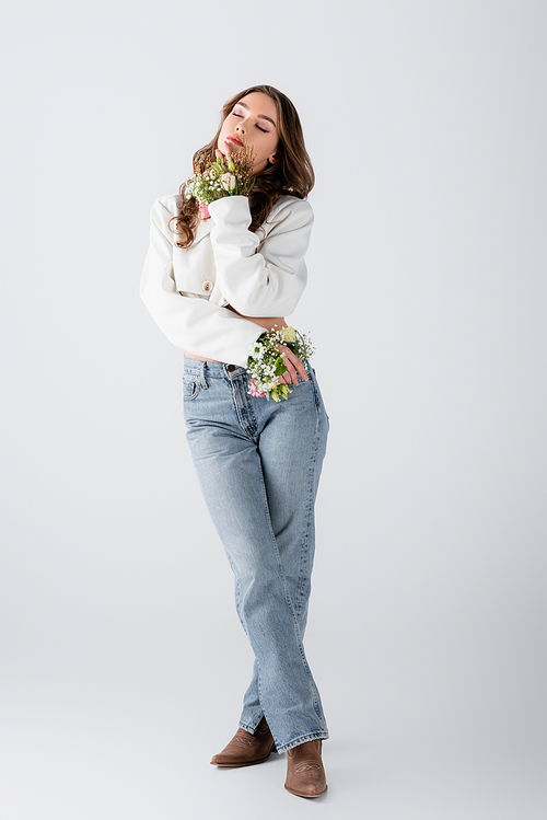 Brunette woman with flowers in sleeves of jacket standing with closed eyes on grey background
