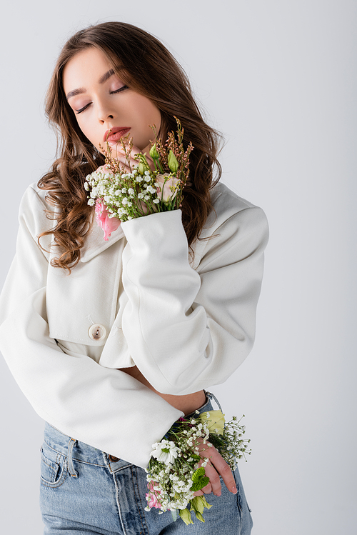 Woman with different flowers in sleeves of jacket posing isolated on grey
