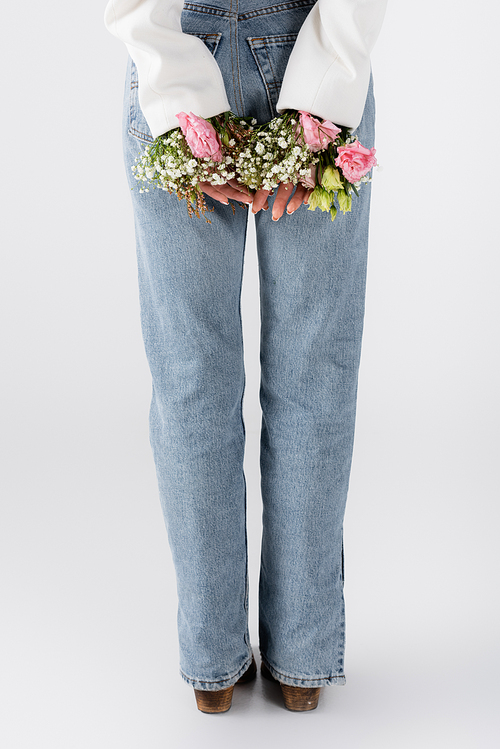 Cropped view of woman in jeans and flowers in jacket on grey