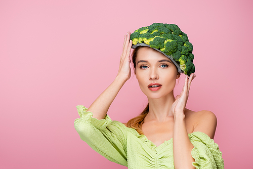 pretty woman touching hat made of fresh broccoli isolated on pink, surrealism concept