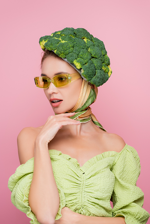 sensual woman in colored eyeglasses and hat made of fresh broccoli isolated on pink, surrealism concept
