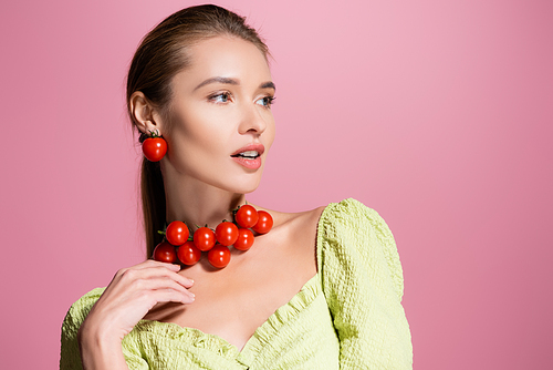 sensual woman in red cherry tomatoes necklace looking away isolated on pink