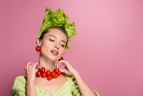 charming woman in lettuce hat, touching necklace mad of cheery tomatoes on pink