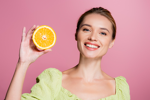joyful woman with natural makeup holding half of fresh orange isolated on pink
