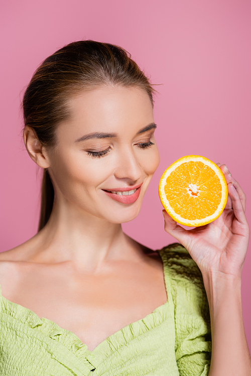 pretty woman with natural makeup holding half of ripe orange isolated on pink