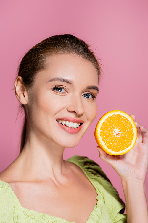 charming woman with natural makeup holding half of ripe orange isolated on pink
