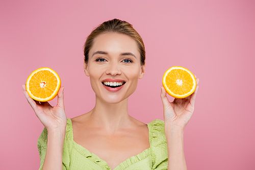 excited woman with natural makeup holding halves of fresh orange isolated on pink