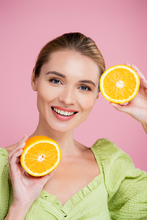 joyful woman with halves of ripe orange smiling at camera isolated on pink