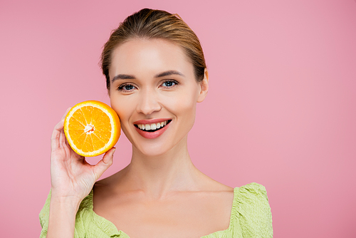 young smiling woman holding half of ripe juicy orange isolated on pink