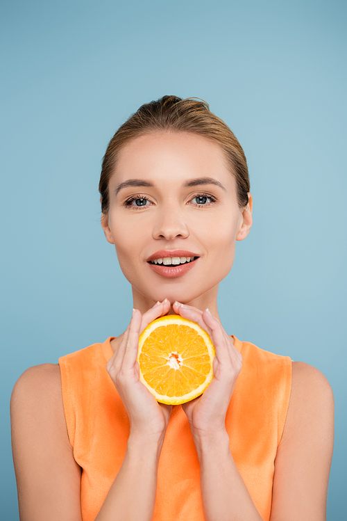 smiling woman with natural makeup holding half of ripe orange isolated on blue