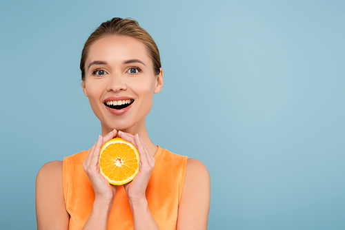 amazed woman with natural makeup holding half of juicy orange isolated on blue