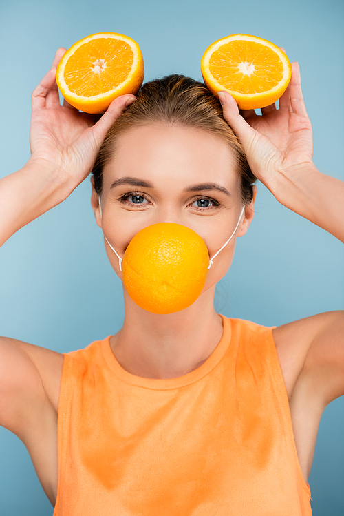young woman in citrus protective mask holding orange halves on blue