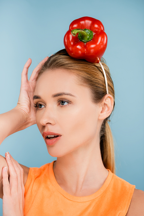 pretty woman with red bell pepper instead of hat looking away isolated on blue