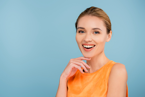 happy woman in orange singlet smiling at camera isolated on blue