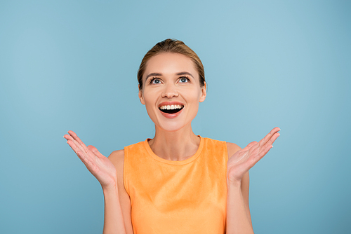 astonished woman with open arms looking up isolated on blue