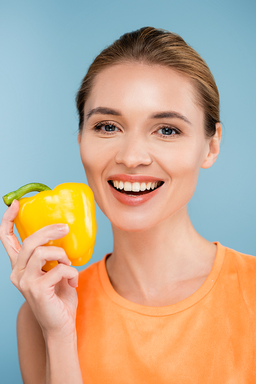 happy young woman with natural makeup posing with bell pepper isolated on blue