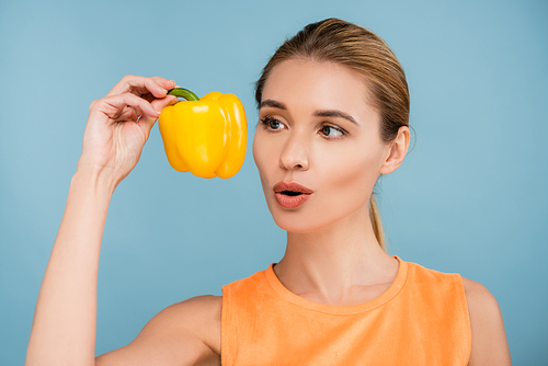 amazed woman with natural makeup holding ripe yellow bell pepper isolated on blue