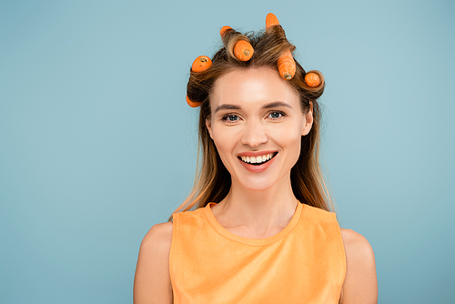 joyful woman  while using carrots instead of curlers isolated on blue