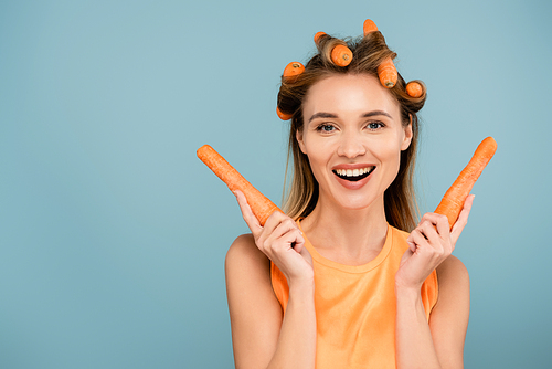 happy young woman  while using carrots instead of curlers isolated on blue