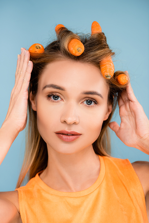 pretty woman with natural makeup using carrots as curlers isolated on blue