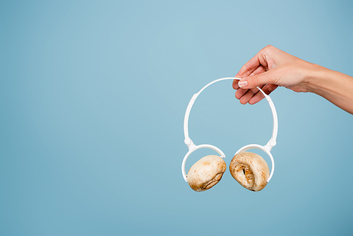 cropped view of woman holding headphones with mushrooms isolated on blue