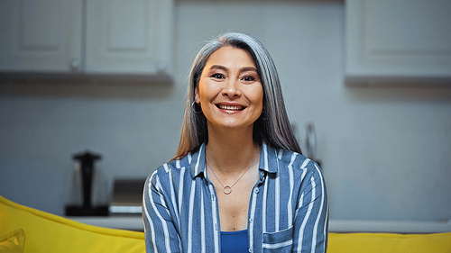 happy senior asian woman in striped shirt smiling at camera at home