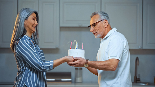 side view of excited asian woman giving birthday cake to senior husband