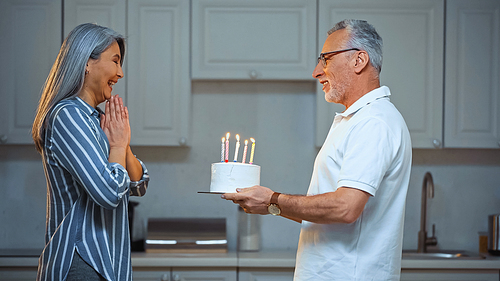 side view of senior man holding birthday cake near astonished asian wife