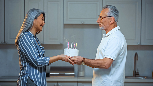 side view of happy senior asian woman taking birthday cake from smiling husband