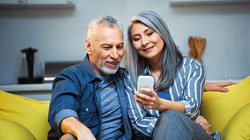smiling asian grey haired woman using smartphone near happy husband