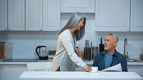 happy grey haired asian woman serving coffee for elderly husband in kitchen