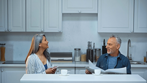 elderly interracial couple talking during morning coffee in kitchen