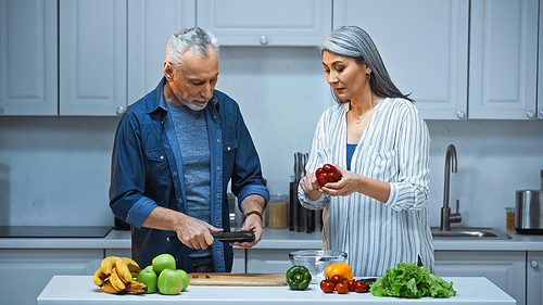 senior interracial couple cutting fresh vegetables in kitchen
