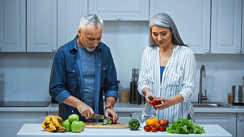 elderly interracial couple preparing fresh salad for breakfast in kitchen