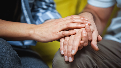 cropped view of woman touching hand on senior husband, blurred background