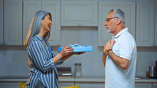 side view of cheerful asian woman presenting gift to amazed elderly husband