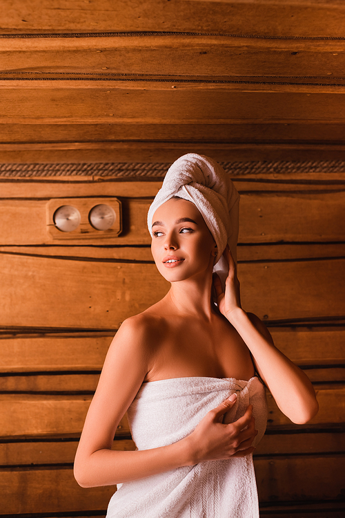 Smiling woman in white towels looking away in wooden sauna