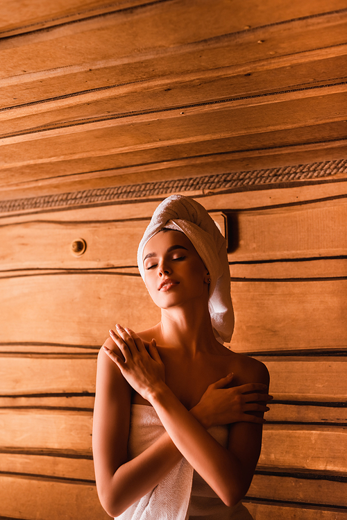 Pleased woman wrapped in towels relaxing in sauna